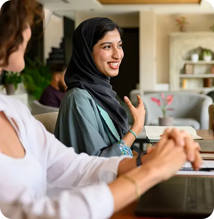 Two professionals in conversation at a table with a laptop and notebook
