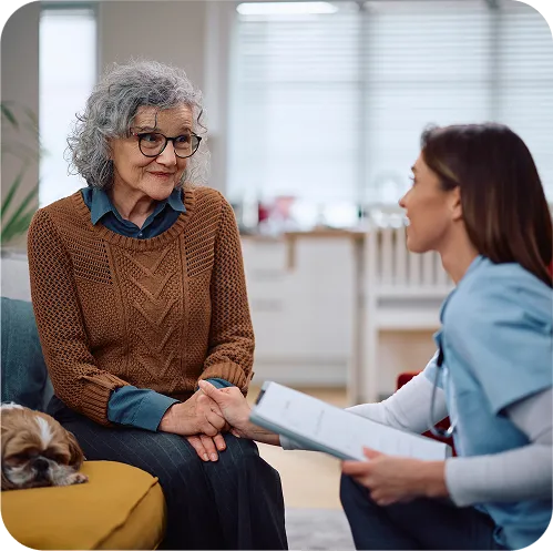 Smiling older woman holding hands with a caregiver who is reviewing paperwork with her at home
