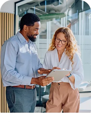 Two smiling colleagues reviewing information together on a tablet